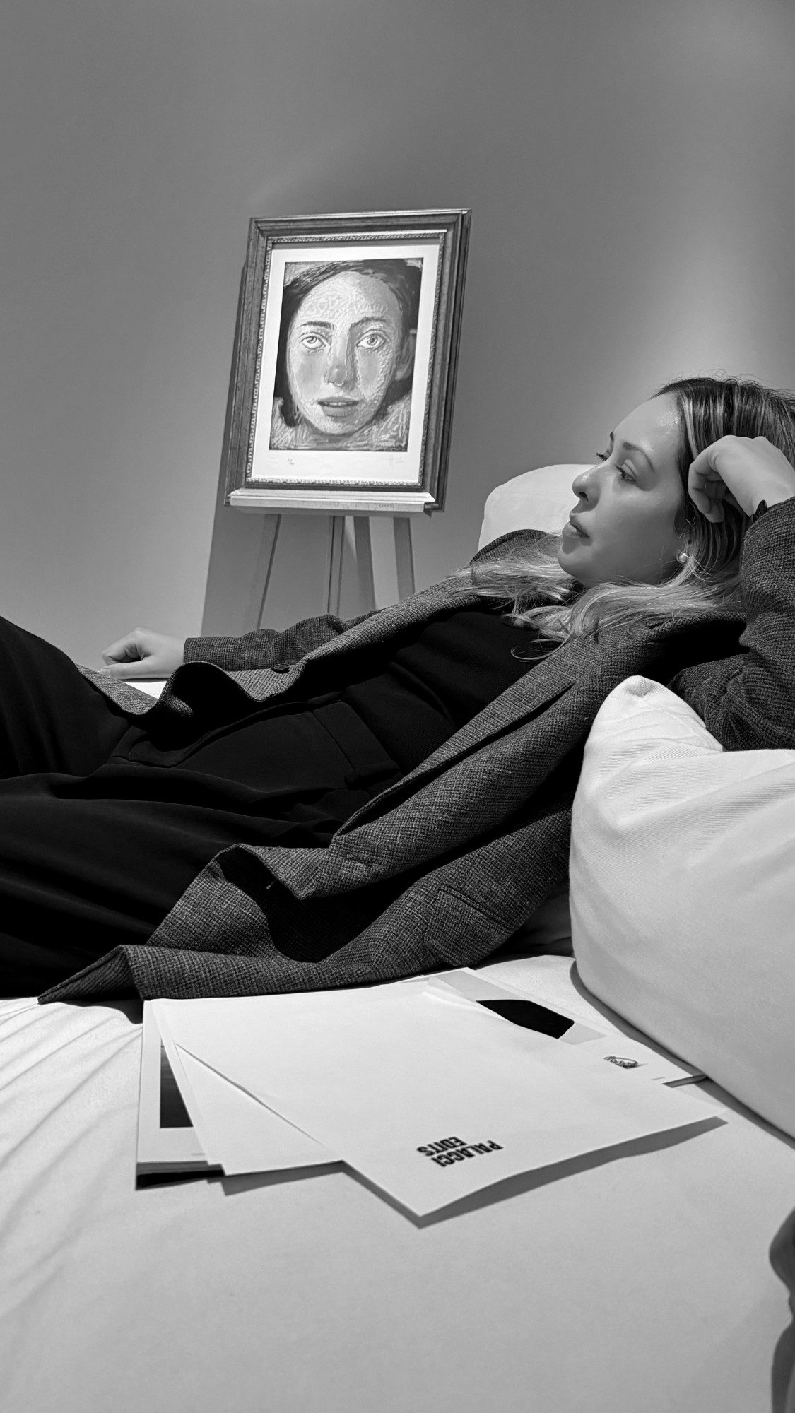 Laura recostada en un sofá blanco junto a un retrato enmarcado, con papeles de Palacci Edits